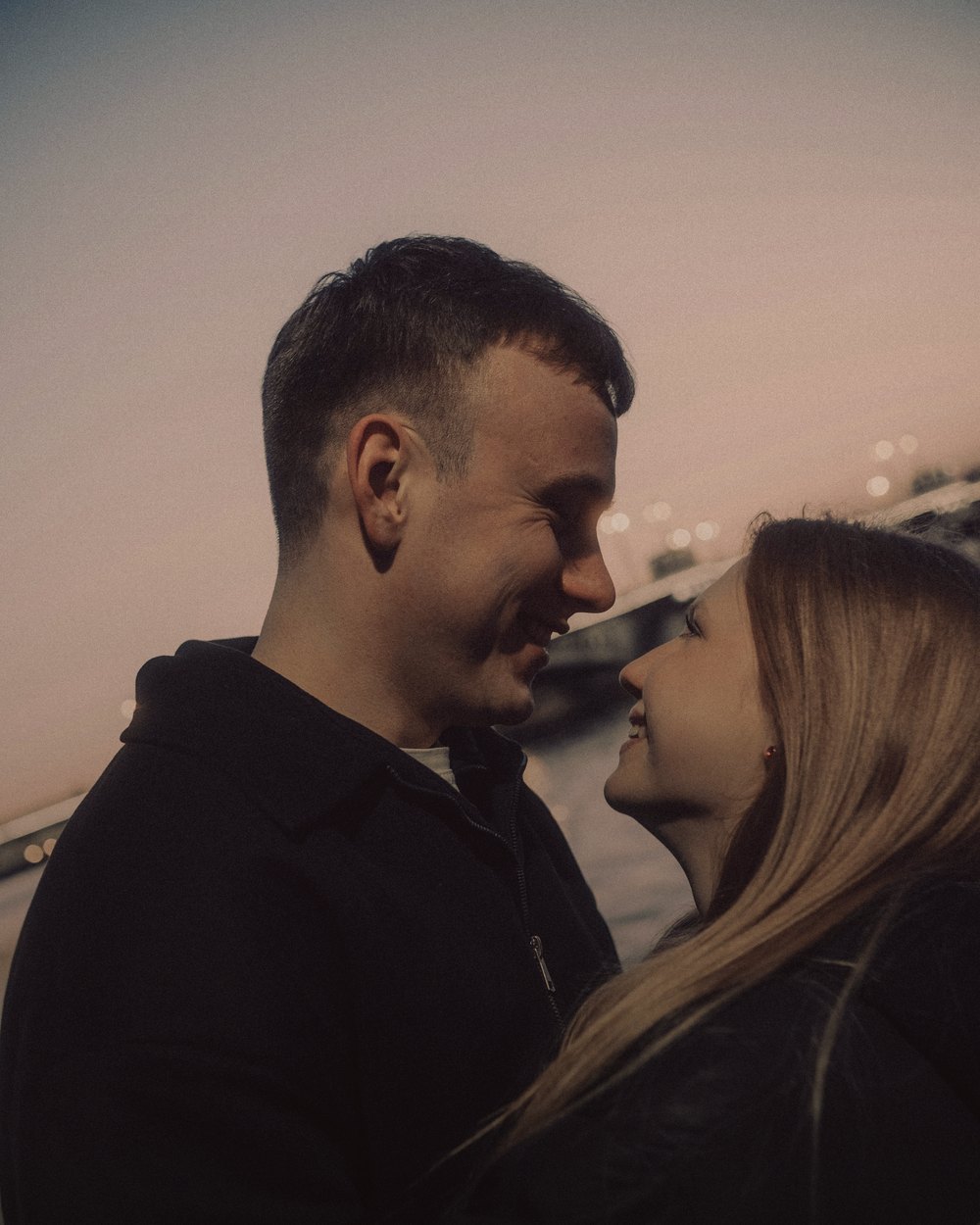 A couple smiling closely together at dusk